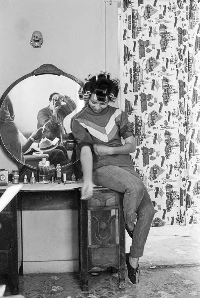 Emmon Clarke's reflection in a mirror while he is taking a photo of a woman in her house. El reflejo de Emmon Clarke through a un espejo mientras toma una foto de una mujer en su casa.