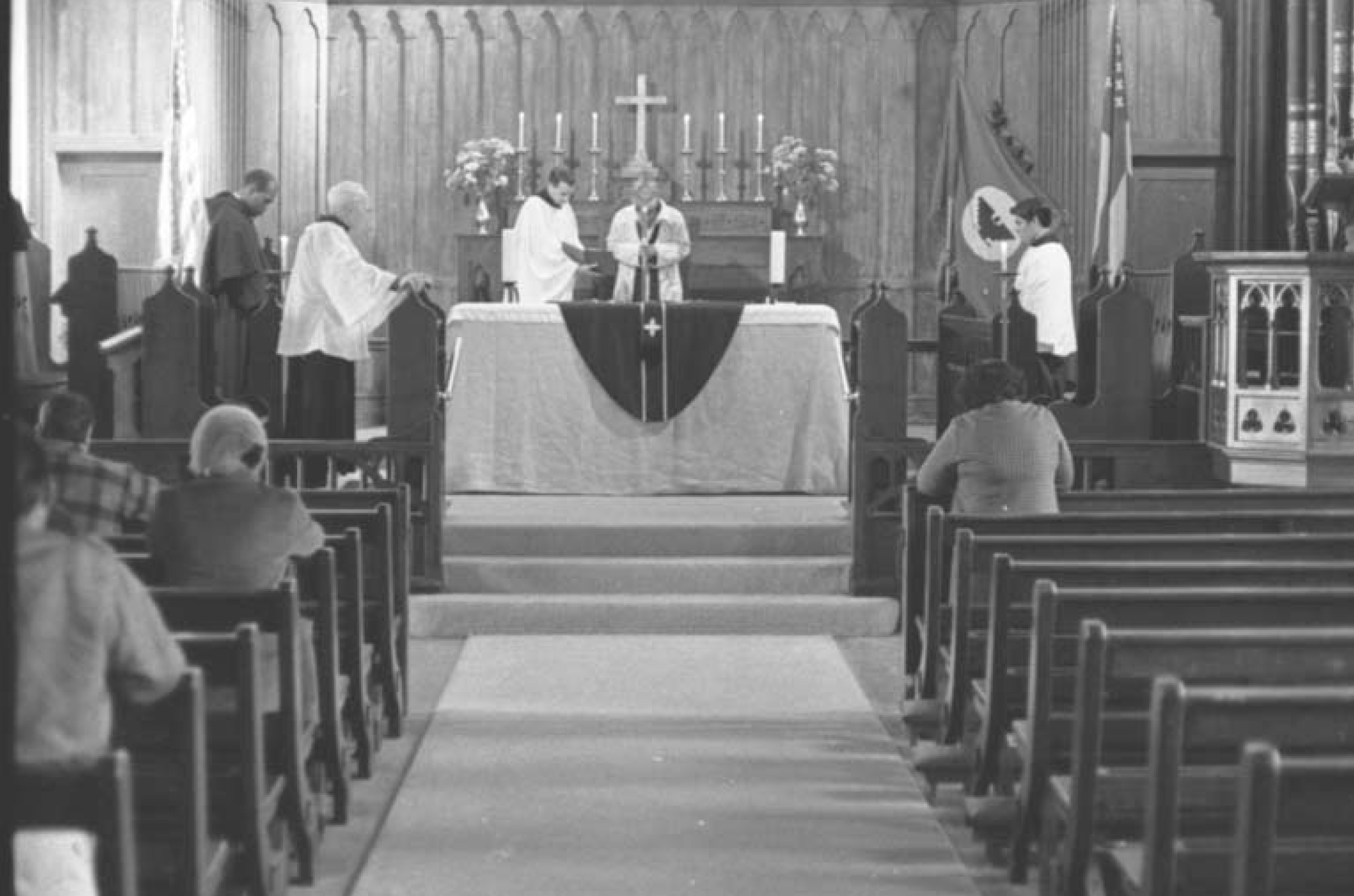 Farmworkers are attending mass by Father John Luce at the Church of the Epiphany in Lincoln Heights. A flag with the black eagle, the symbol of the farmworker movement, is visible next to the altar