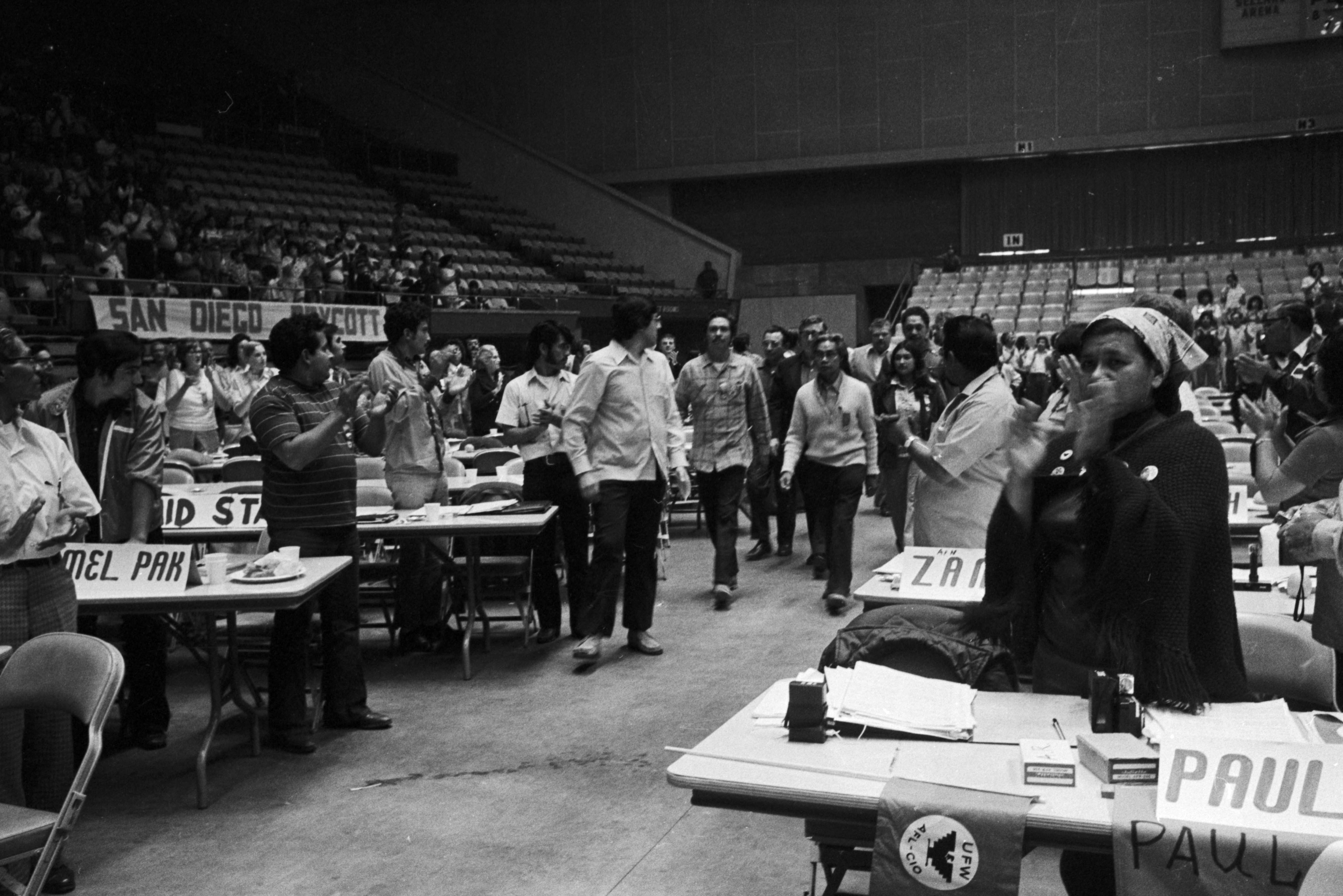 UAW president Leonard Woodcock (center, behind Philip Vera Cruz, wearing a dark suit and glasses) and Philip Vera Cruz (center, wearing a white sweater) walk on the floor of the UFW's First Constitutional Convention at Fresno Convention Center's Selland Arena in Fresno, California. El presidente de UAW Leonard Woodcock (centro, detrás de Philip Vera Cruz, con traje oscuro y anteojos) y Philip Vera Cruz (centro, con suéter blanco) caminan en el piso de la Primera Convención Constitucional de la UFW en el Selland Arena del Centro de Convenciones de Fresno en Fresno, California.