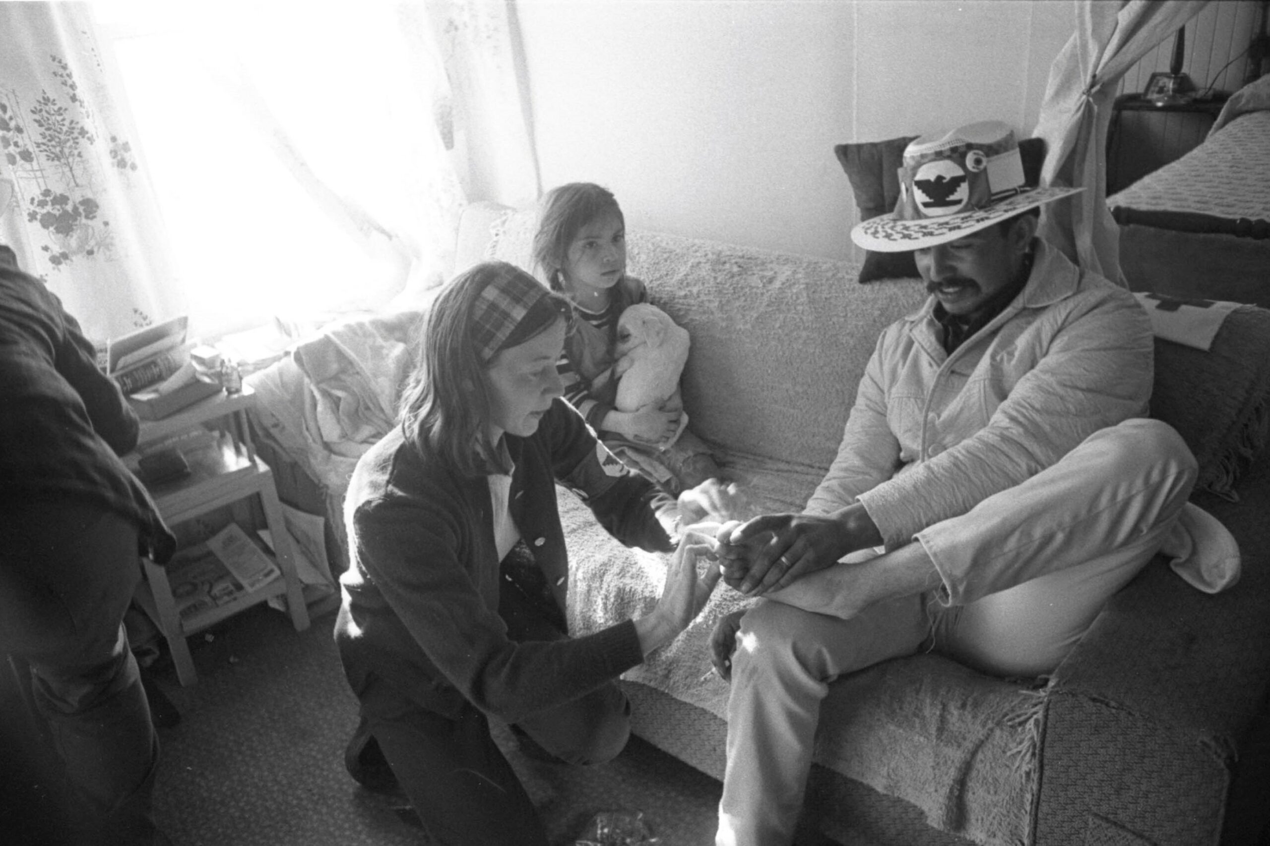 Nurse Peggy McGivern inspects the feet of a marcher sitting inside a house during the march to Sacramento, 1966